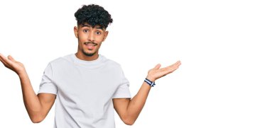 Gündelik beyaz tişört giyen genç Arap adam gülümseyerek avuçlarını açıyor, sunuyor ve reklam karşılaştırması yapıyor ve dengeyi sağlıyor. 