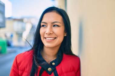 Genç Latin kadın gülümsüyor. Şehrin duvarına yaslanmaktan mutlu..