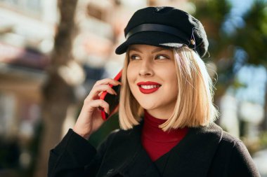 Genç sarışın kadın gülümsüyor. Şehirdeki akıllı telefondan konuşuyor..