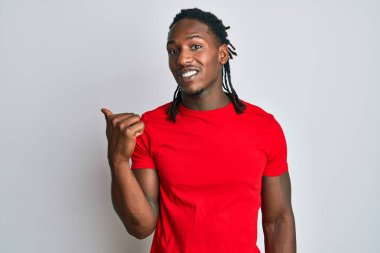 Saçları örgülü, mutlu yüzüyle gülümseyen ve baş parmağıyla yüzünü gösteren Afro-Amerikan bir adam.. 