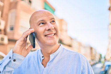 Orta yaşlı kel adam gülümsüyor. Şehirdeki akıllı telefondan mutlu mesut konuşuyor..