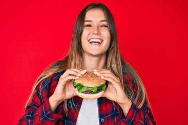 Güzel, beyaz bir kadın lezzetli bir klasik burger yiyor ve kahkahalarla gülüyor çünkü komik, çılgınca bir şaka.. 