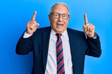 İş elbisesi ve kravat takan kıdemli beyaz adam şaşırmış, şaşırmış ve parmaklarıyla işaret ediyor ve kollarını kaldırıyordu.. 