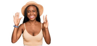 Genç siyah kadın yaz şapkası takıyor ve 8 numaralı parmaklarıyla işaret ederken kendinden emin ve mutlu bir şekilde gülümsüyor.. 