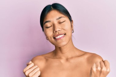 Genç Çinli kadın üstsüz duruyor. Çok mutlu ve heyecanlı görünüyor. Kolları havada, gülümseyen ve başarı için çığlık atan kazanan bir jest yapıyor. kutlama konsepti. 