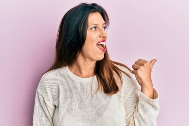 Güzel İspanyol kadın, gündelik giysiler giyip baş parmağını yana kaldırıyor ve ağzı açık gülümsüyor. 