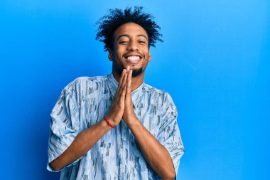 Sakallı, sıradan giyinmiş, elleriyle dua eden, affedilmek isteyen, kendinden emin gülümseyen Afro-Amerikalı genç bir adam.. 