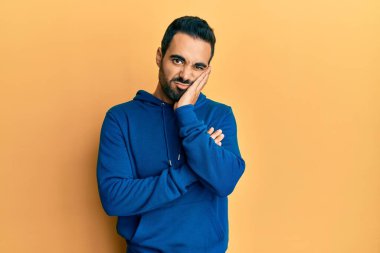 Günlük kıyafetler giyen genç İspanyol adam kollarını kavuşturarak depresyondan sıkılmış ve yorgun görünüyor.. 