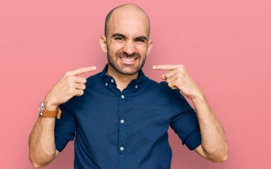 Günlük kıyafetler giyen, neşeli gülümseyen, parmaklarıyla ve ağzıyla işaret eden İspanyol genç bir adam. diş sağlığı kavramı. 