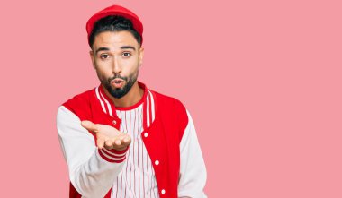 Beyzbol forması giyen sakallı genç adam kameraya bakıp havada bir öpücük savuruyor ve sevimli ve seksi oluyor. aşk ifadesi. 