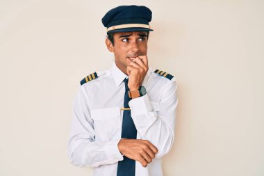 Uçak pilotu üniforması giyen genç İspanyol adam gergin görünüyor ve elleri ağızda tırnak yiyor. anksiyete. 