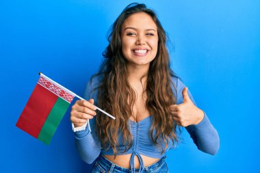 Beyaz bayrak tutan genç İspanyol kız mutlu ve pozitif gülümsüyor, başparmağıyla mükemmel ve onay işareti yapıyor. 