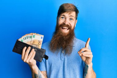 Uzun sakallı, elinde cüzdanı olan kızıl saçlı bir adam. Avro banknotları gülümsüyor. 