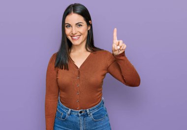 Genç İspanyol kadın gündelik kıyafetler giyip bir numarayı gösterip işaret ederken kendinden emin ve mutlu bir şekilde gülümsüyor.. 