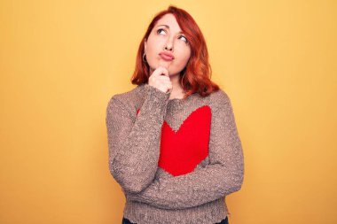 Genç, güzel, kızıl saçlı bir kadın, sarı arka planda kalbi olan, gündelik bir süveter giyiyordu. Kuşkuya odaklanmıştı.