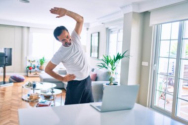 Orta yaşlı, sakallı ve esnek bir adam evde egzersiz yapıyor bilgisayardaki spor videolarına bakıyor.