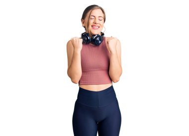 Güzel beyaz kadın spor kıyafetleri giyiyor ve kulaklık takıyor. Başarı için heyecanlanıyor. Kolları havada ve gözleri kapalı zaferi kutluyor. Kazanan konsept. 