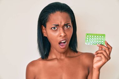 Genç Afro-Amerikalı kadın şok olmuş suratında doğum kontrol hapları tutuyor. Şüpheci ve alaycı görünüyor. 