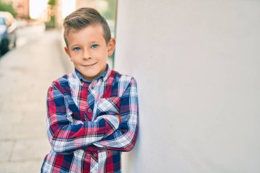 Kollarını kavuşturup gülümseyen sevimli beyaz çocuk şehrin duvarına yaslanmış mutlu..