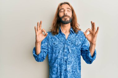 Uzun saçlı ve sakallı çekici bir adam 80 'lerin disko tarzı tişörtünü giyiyor rahat ve gözleri kapalı gülümsüyor parmaklarıyla meditasyon hareketi yapıyor. yoga konsepti. 