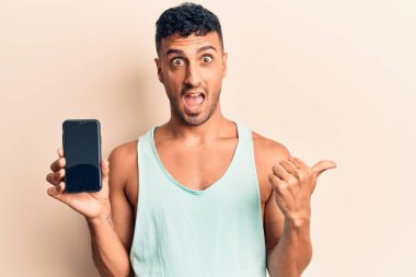 Genç İspanyol adam akıllı telefon tutuyor. Ekranı işaret ediyor. Parmağını yana kaldırıyor. 