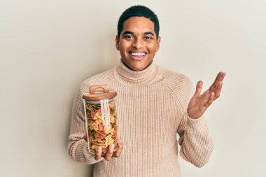 Genç, yakışıklı İspanyol adam elinde kavanozla farfalle makarna ile başarıyı kutluyor mutlu bir gülümsemeyle ve kazanan yüz ifadesiyle elini kaldırarak. 