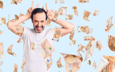 Orta yaşlı yakışıklı bir adam günlük tişört giyiyor komik ve deli pozu veriyor parmakları tavşan kulağı gibi, neşeli gülümsüyor.