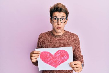 Kalbi olan yakışıklı beyaz bir adam komik suratıyla pofuduk yanaklar çiziyor. Ağzı havayla şişer, havayı yakalar.. 