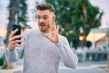 Kafkasyalı genç adam şehirde akıllı telefon kullanarak video araması yaparken mutlu gülümsüyor..