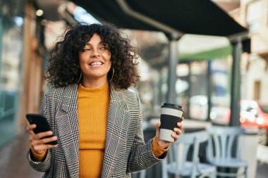 Genç İspanyol iş kadını akıllı telefon kullanıyor. Şehirde kahve içiyor..