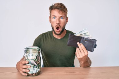 Cüzdanı dolar ve kavanozla dolu genç beyaz bir adam masanın üzerinde korku ve şaşkınlık dolu bir ifadeyle korku ve heyecan dolu bir yüzle oturuyor.. 