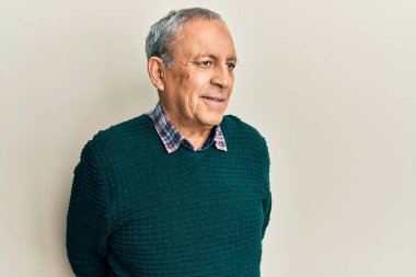 Gri saçlı, sıradan bir süveter giyen yakışıklı, rahat bir görünüm takınan, kendine güvenen ve gülümseyen bir adam.. 