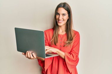 Bilgisayarla çalışan genç ve güzel bir kadın pozitif ve mutlu görünüyor. Kendine güvenen bir gülümsemeyle ayakta duruyor ve dişlerini gösteriyor. 