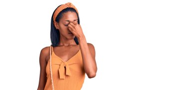 Genç Afrikalı Amerikalı kadın yaz kıyafeti giyip burnu ve gözleri ovuşturmaktan yorgun düşmüş. Yorgunluk ve baş ağrısı çekiyor. Stres ve hüsran kavramı. 