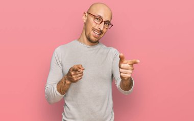 Sıradan kıyafetler giyen ve gözlüklü kel bir adam mutlu ve komik yüzüyle kamerayı işaret ediyor. iyi enerji ve titreşimler. 