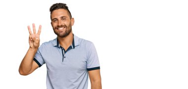 Sakallı, sıradan kıyafetler giyen, üç numaralı parmaklarıyla işaret eden, kendinden emin ve mutlu gülümseyen yakışıklı bir adam.. 