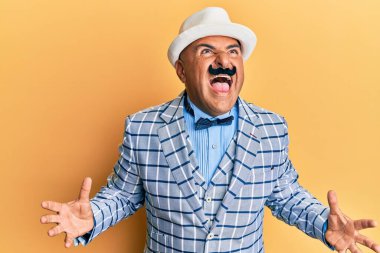 Klasik ve zarif moda tarzı olan bıyıklı olgun bir Orta Doğulu çılgın ve sinirli bir şekilde bağırıyor ve agresif bir ifadeyle kollarını kaldırıyor. hüsran kavramı. 