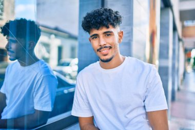 Genç Arap adam gülümsüyor. Şehrin duvarına yaslanıyor..