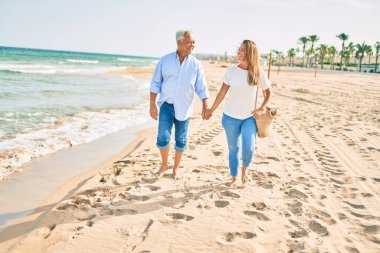 Orta yaşlı İspanyol çift kumsalda yürürken mutlu bir şekilde gülümsüyor..