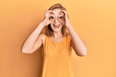 Kolsuz tişörtlü, sıradan giyinen genç, beyaz bir kadın dürbün gibi güzel hareketler yapıyor, gözleri parmaklarından bakıyor. çılgın ifade. 