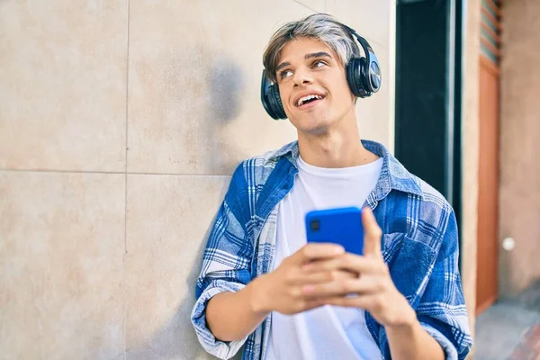 Young hispanic man smiling happy using smartphone and headphones at the city.