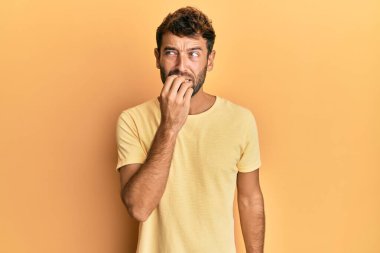 Sarı arka planda sıradan sarı tişörtler giyen sakallı yakışıklı adam gergin ve elleri ağız yiyen tırnaklarıyla gergin görünüyor. anksiyete. 