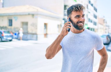 Genç İspanyol adam şehirde akıllı telefon kullanarak mutlu bir şekilde gülümsüyor.