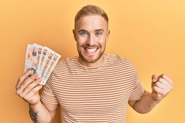 Kafkasyalı genç adam elinde 10 pound tutuyor gururla bağırıyor, zaferi ve başarıyı kutluyor. 