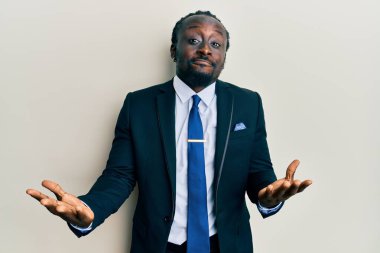 Yakışıklı, takım elbiseli, kravatlı, budala ve kafası karışmış elleri ve kolları havada genç bir zenci. şüphe kavramı. 