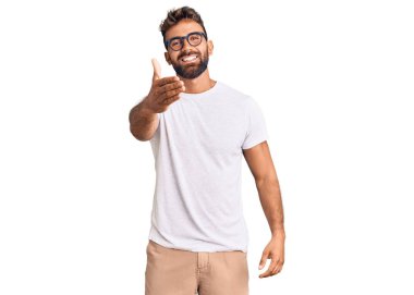 Gündelik kıyafetler ve gözlük takan genç İspanyol adam dostça bir selamlama ve hoş geldin hediyesi olarak el sıkışmayı sunuyor. başarılı iş. 