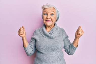 Kış şapkası ve yün kazak giyen yaşlı gri saçlı kadın gururla haykırıyor, zaferi kutluyor ve başarıyı kollarını kaldırarak kutluyor. 