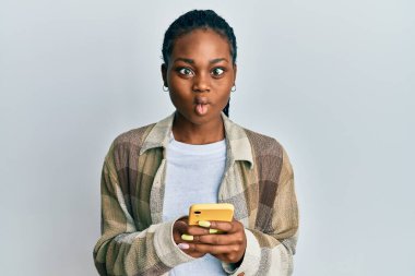 Genç Afrikalı Amerikalı kadın akıllı telefon kullanıyor. Ağızlı balık suratı yapıyor ve şaşı bakıyor. Deli ve komik.. 