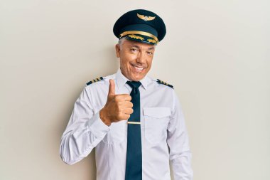 Yakışıklı, orta yaşlı, uçak pilotu üniforması giyen olgun bir adam mutlu bir el hareketi yapıyor. Kameraya bakıp başarıyı gösteren ifade. 