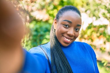 Genç Afrikalı Amerikalı kadın mutlu bir şekilde gülümsüyor. Parktaki kameranın önünde selfie çekiyor..